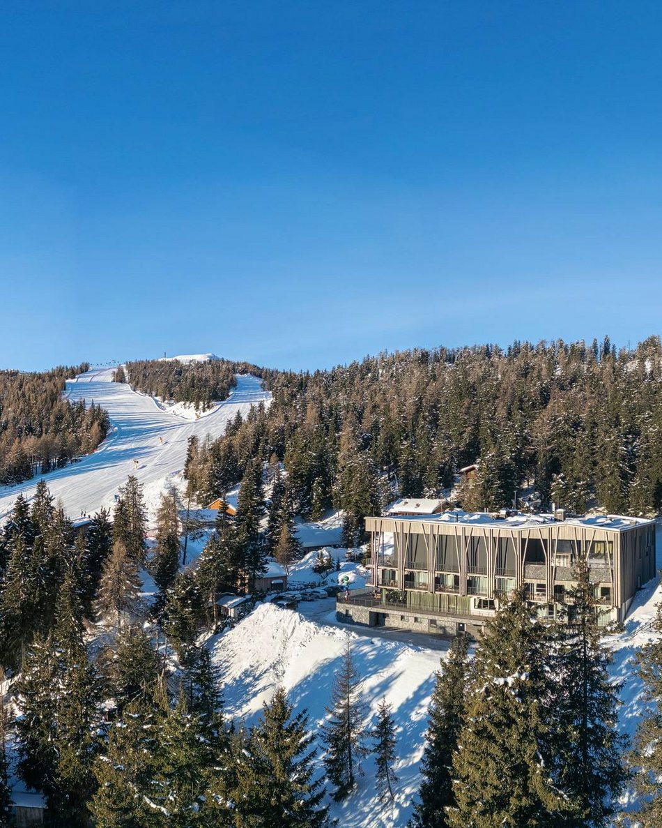 Dein Hotel im Pustertal: Olangerhof Winterlandschaft mit Skipisten, Bäumen und modernem Gebäude in den Bergen