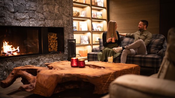 Dein Hotel in Olang: Willkommen im Olangerhof! Paar unterhält sich auf Sofa neben brennendem Kamin in gemütlichem Wohnzimmer