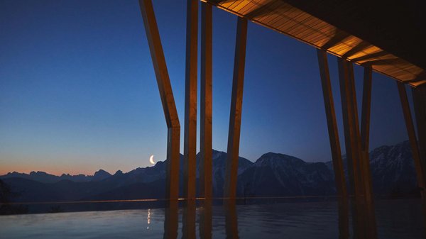 Dein Wellnesshotel am Kronplatz: Olangerhof Zunehmender Mond über schneebedeckten Bergen, gesehen von einer Holzstruktur bei Dämmerung