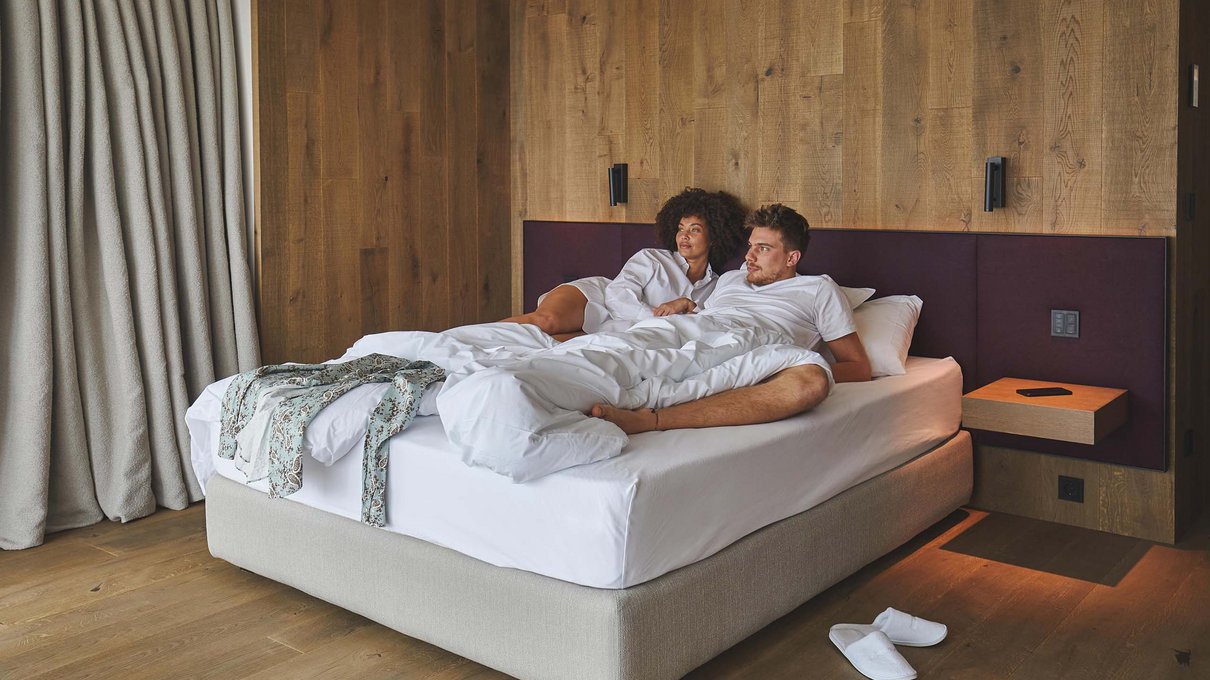 Deine Unterkunft im Pustertal: oh, wow! Paar liegt auf weißem Bett in Zimmer mit Holzwänden