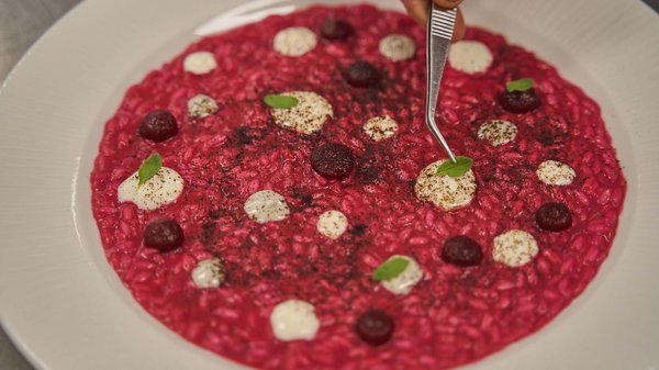 Hotels an der Piste in Südtirol mit Halbpension Roter Risotto mit weißer Creme, grünen Blättern und Garnitur