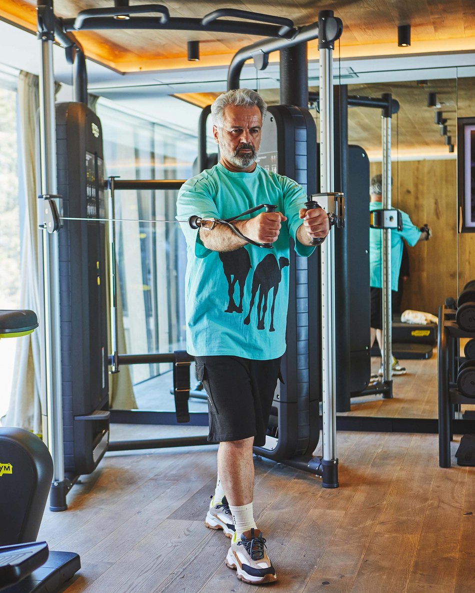 Kronplatz/Südtirol: Hotels Älterer Mann trainiert mit Kabelgerät in modernem Fitnessraum