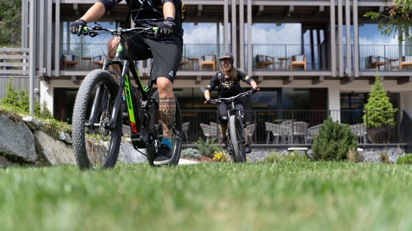 Dein Hotel in Olang: Willkommen im Olangerhof! Zwei Personen fahren mit E-Bikes vor einem modernen Gebäude