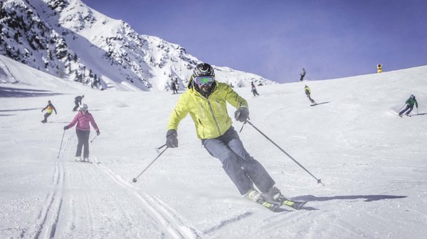 Kronplatz + Hotel an der Piste = Olangerhof Skifahrer in gelber Jacke auf verschneiter Piste mit Bergkulisse