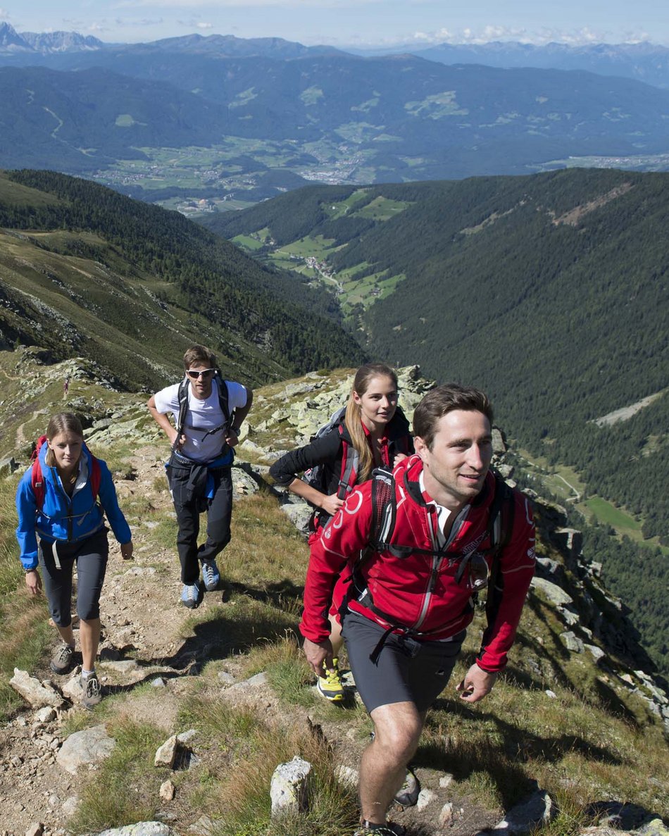 Olang in summer: sunny days at Olangerhof Four hikers walking up a mountain trail with scenic alpine valleys below