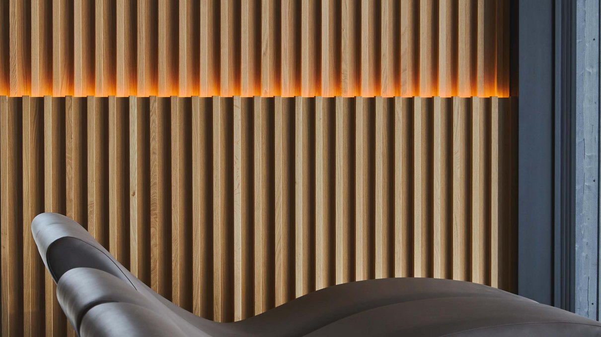 Deine Unterkunft im Pustertal: oh, wow! Moderne wellenförmige Sessel neben einer Holzwand mit warmer Beleuchtung