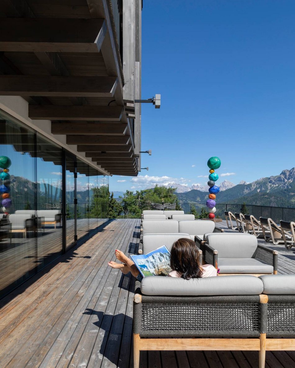 Dein Hotel in Olang: Willkommen im Olangerhof! Terrasse mit Sofas und Bergblick, eine Person liest ein Buch