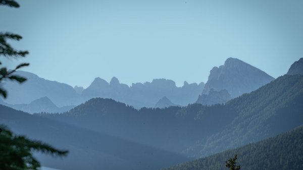 Dein Hotel in Olang: Willkommen im Olangerhof! Gebirgskette mit bewaldeten Hügeln unter klarem blauem Himmel