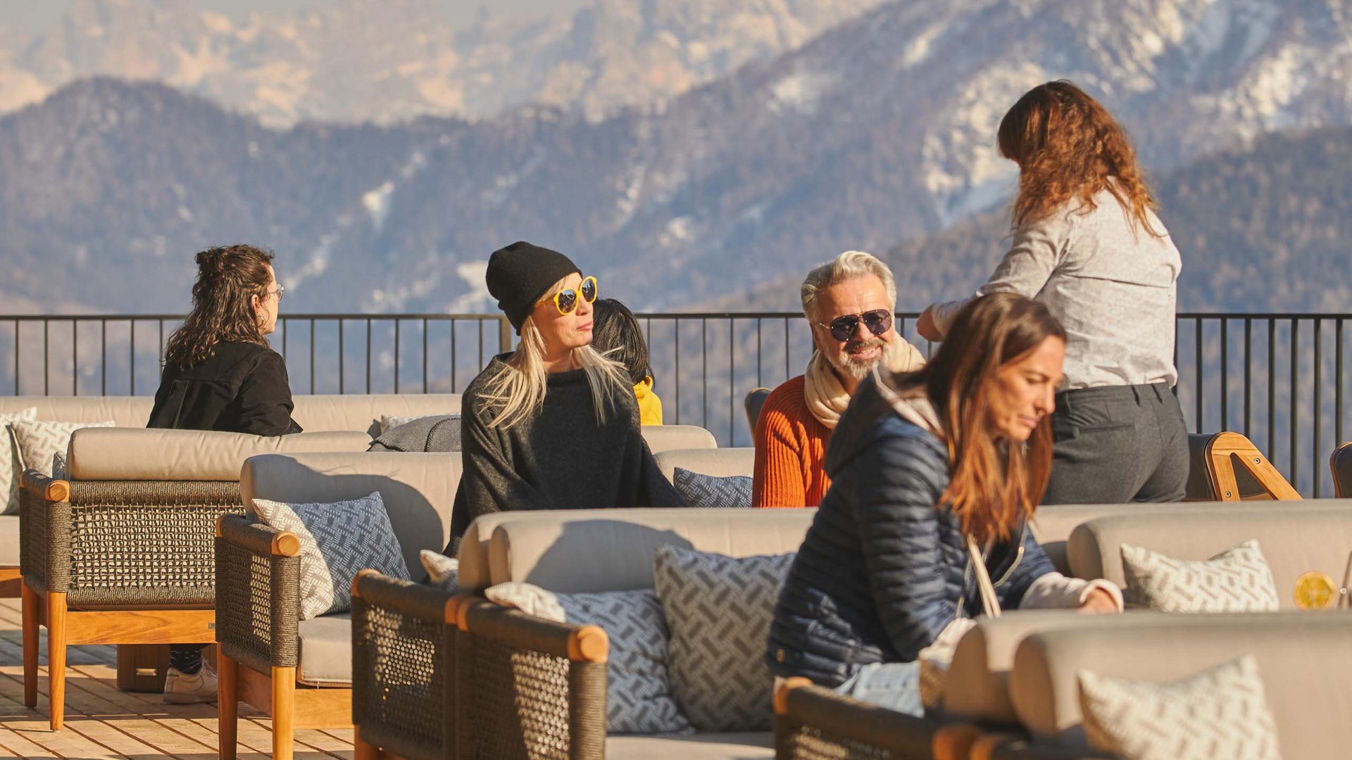 Hotels in Olang gesucht? Menschen sitzen auf einer Terrasse mit Blick auf verschneite Berge