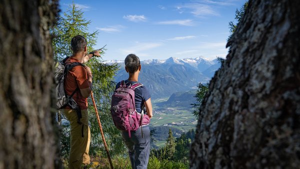 Dein Hotel in Olang: Willkommen im Olangerhof! Zwei Wanderer blicken und zeigen auf ein Bergtal unter klarem Himmel
