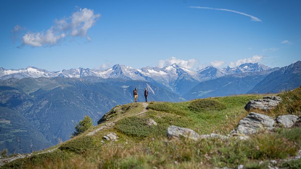 Dein Hotel in Olang: Willkommen im Olangerhof! Zwei Personen stehen auf einem Hügel mit Blick auf schneebedeckte Berge