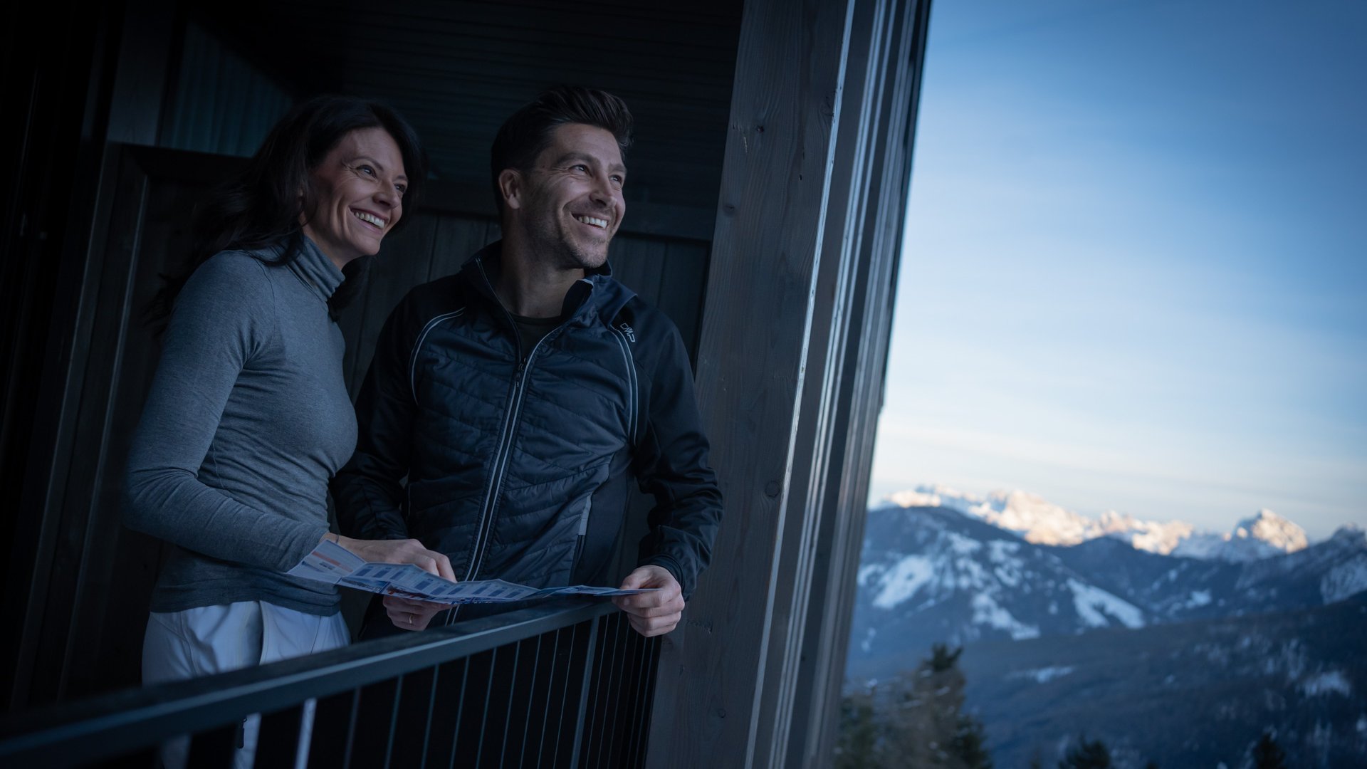 Olang in Südtirol: Wanderungen Lächendes Paar blickt auf eine Karte auf Balkon mit Blick auf schneebedeckte Berge