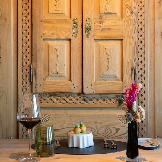 Hotels an der Piste in Südtirol mit Halbpension Rustikaler Tisch mit Weinglas, Gourmetgericht und Vase mit Trockenblumen
