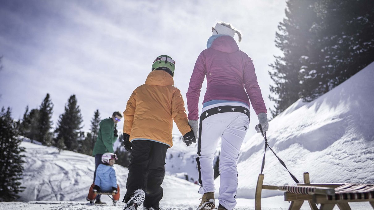 Deine Unterkunft im Pustertal: oh, wow! Familie wandert mit Schlitten im sonnigen Schnee in den Bergen
