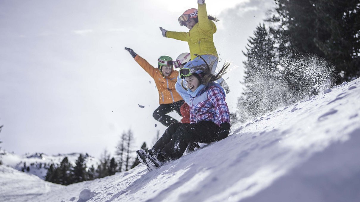 Deine Unterkunft im Pustertal: oh, wow! Vier Jugendliche rutschen lachend einen schneebedeckten Hang hinunter