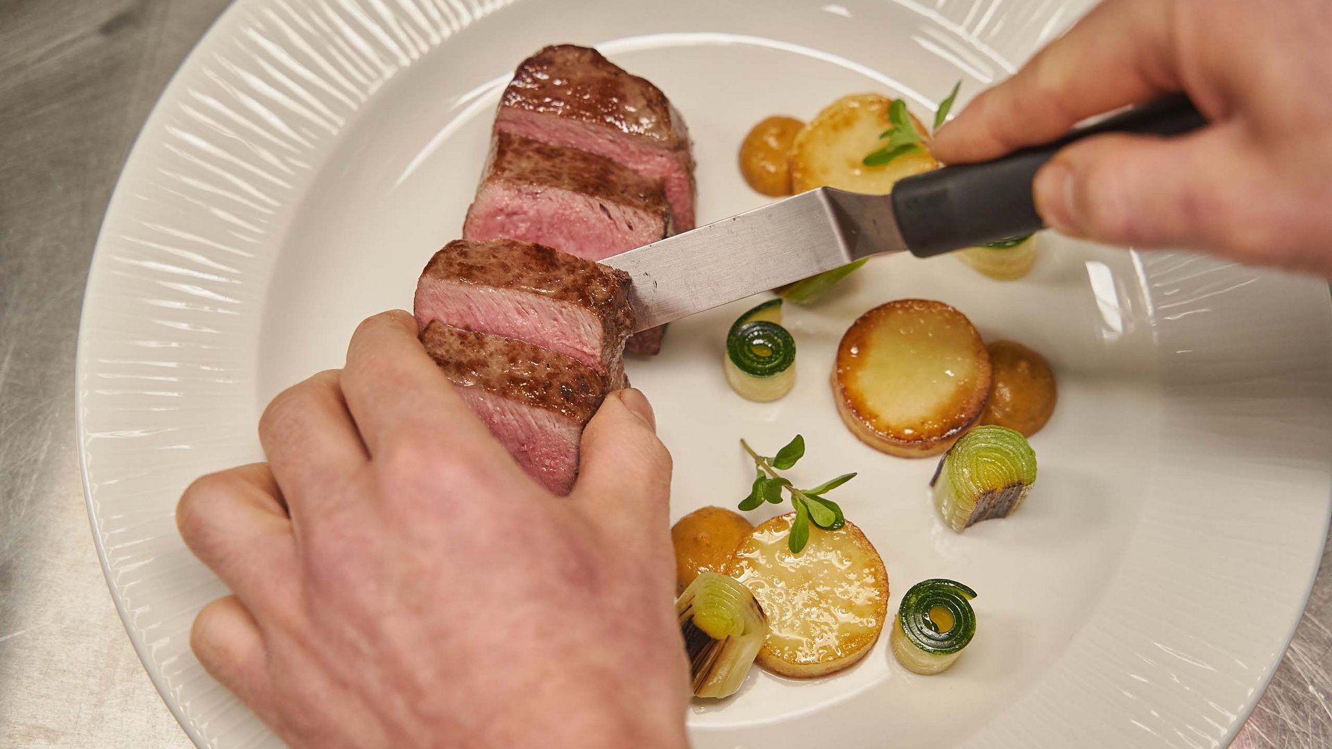 Hotel near Plan de Corones/Kronplatz: more flavour! Hand cutting medium steak with sides on a white plate