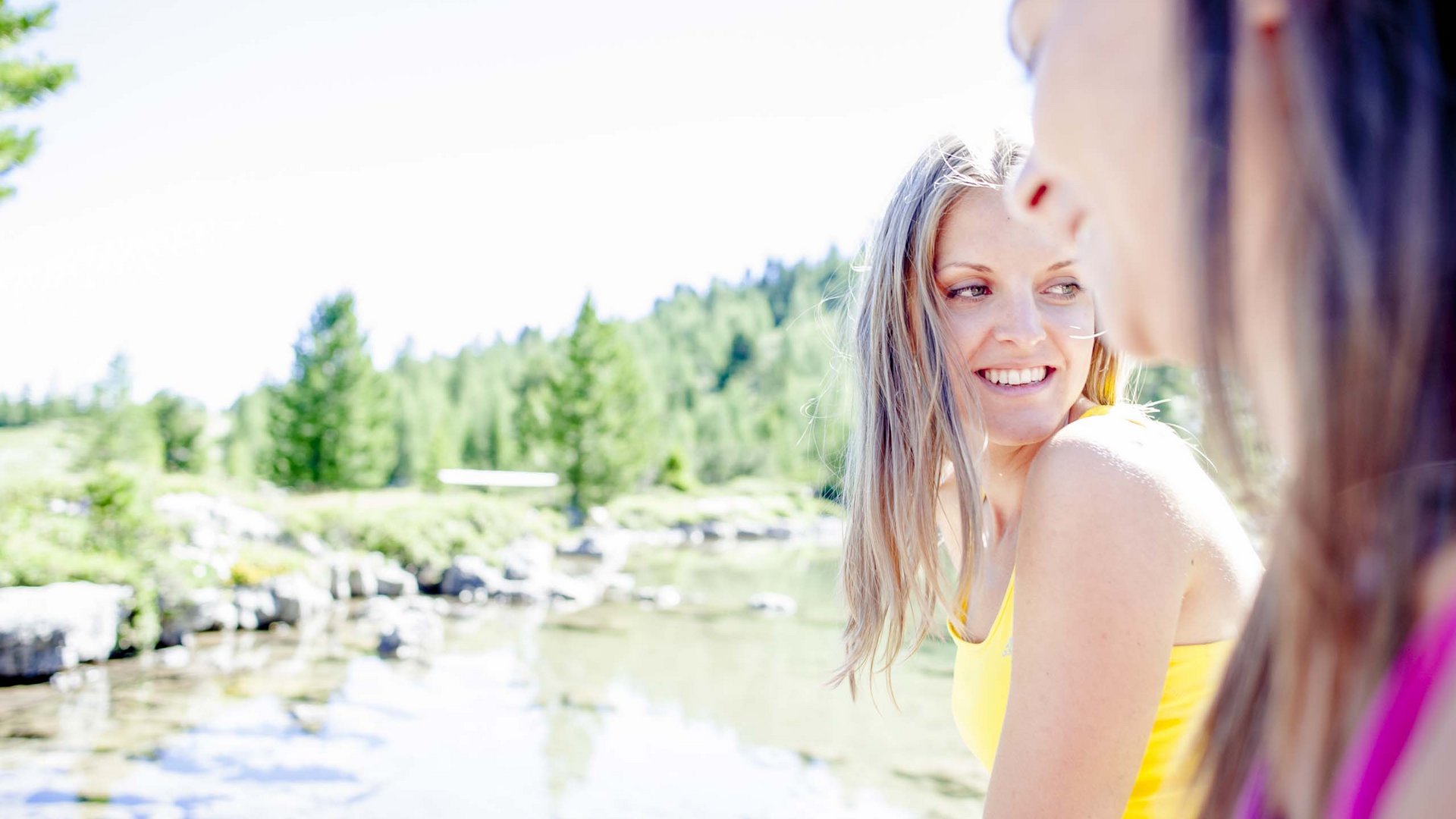Escursioni a Valdaora nei pressi dell’Olangerhof Due donne sorridenti vicino a un lago con alberi sullo sfondo