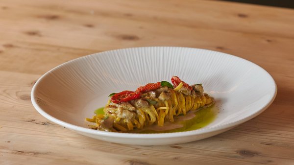 Hotels an der Piste in Südtirol mit Halbpension Eleganter Teller mit gerollter Pasta, getrockneten Tomaten und grüner Sauce auf Holztisch