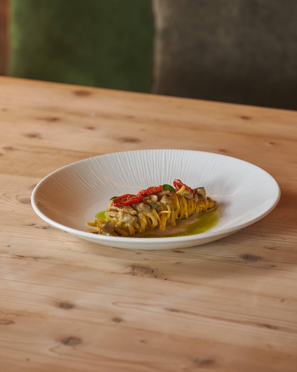 Unterkünfte in Olang: Komm auf den Geschmack! Eleganter Teller mit gerollter Pasta, getrockneten Tomaten und grüner Sauce auf Holztisch