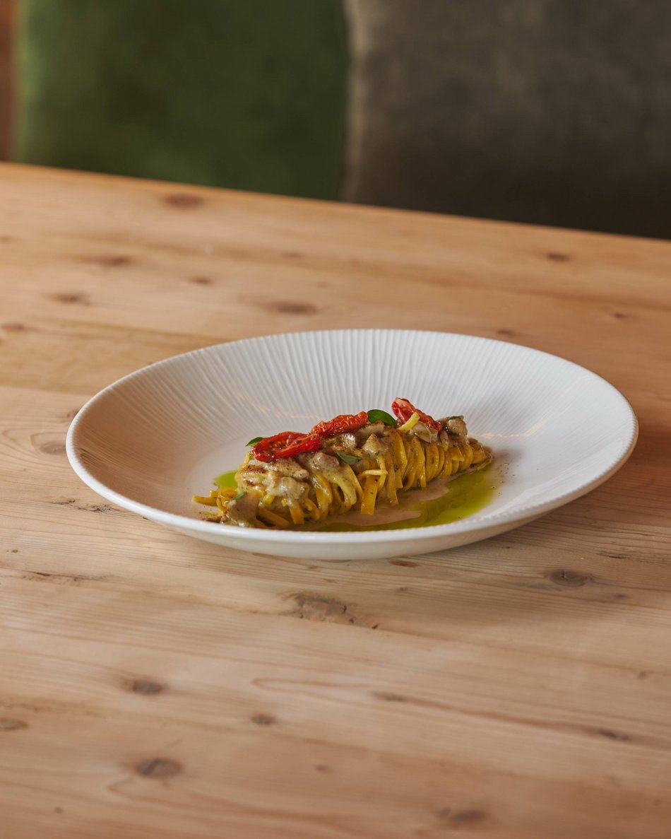 Hotel near Plan de Corones/Kronplatz: more flavour! Elegant plate with rolled pasta, sun-dried tomatoes, and green sauce on wooden table