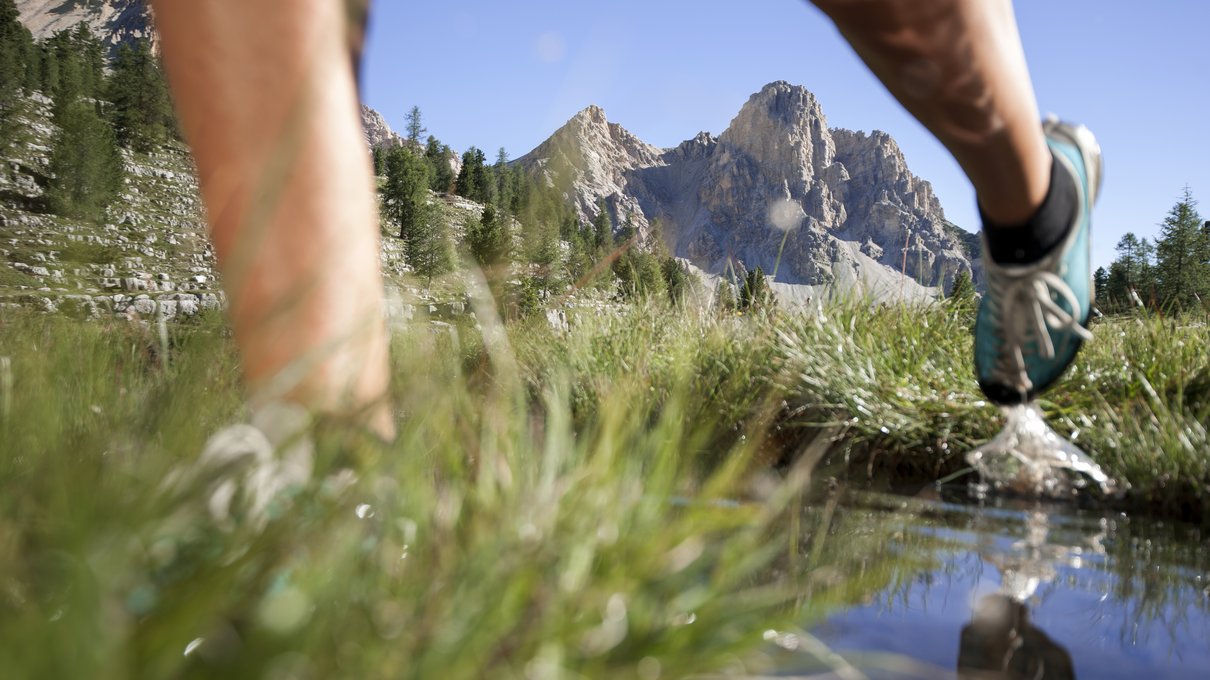Deine Unterkunft im Pustertal: oh, wow! Blaue Laufschuhe laufen auf bergigem Grasweg mit Teich und Bergen im Hintergrund