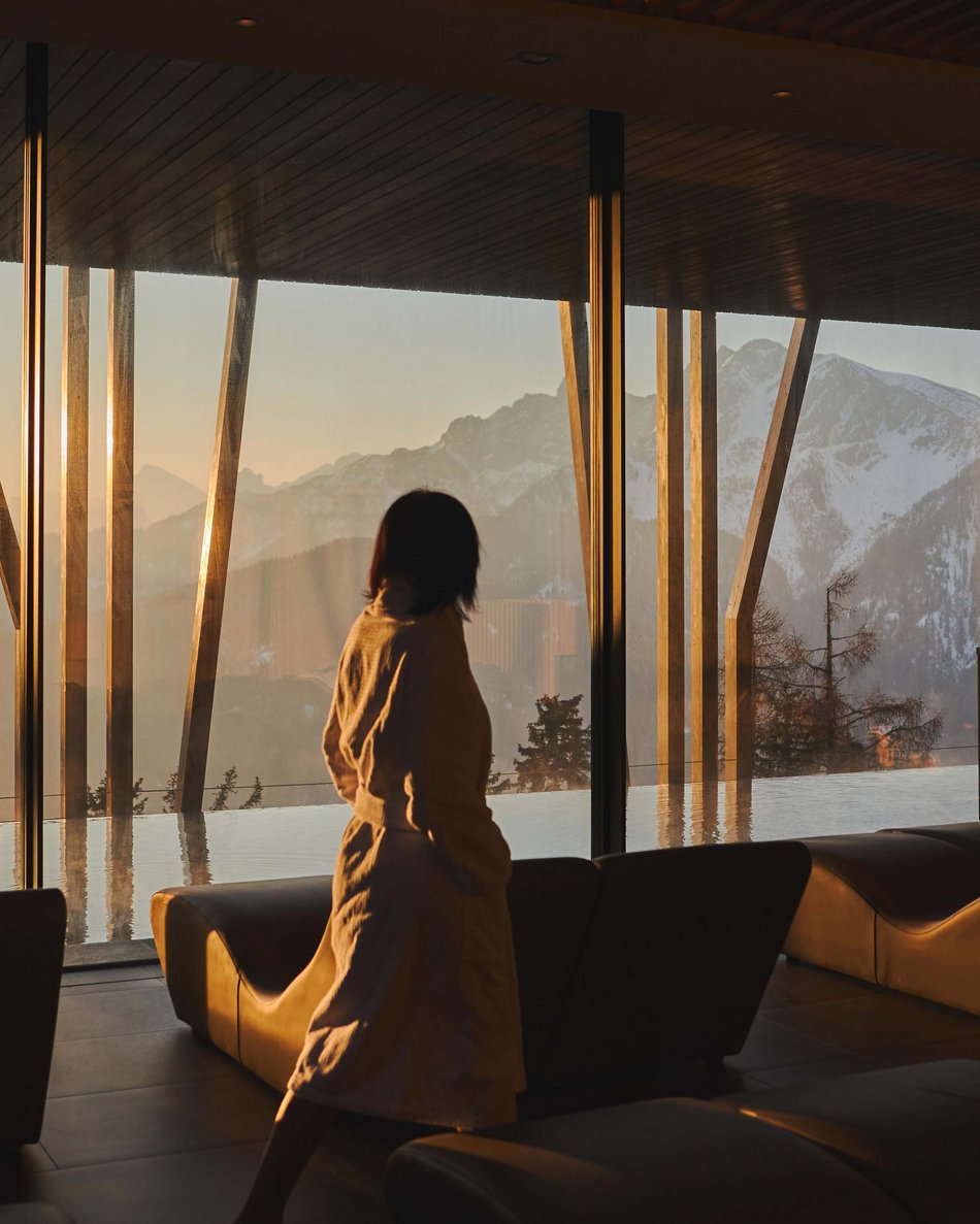 Hotel in Plan de Corones con piscina: il tuo Olangerhof Persona in accappatoio che guarda verso montagne innevate attraverso grandi finestre