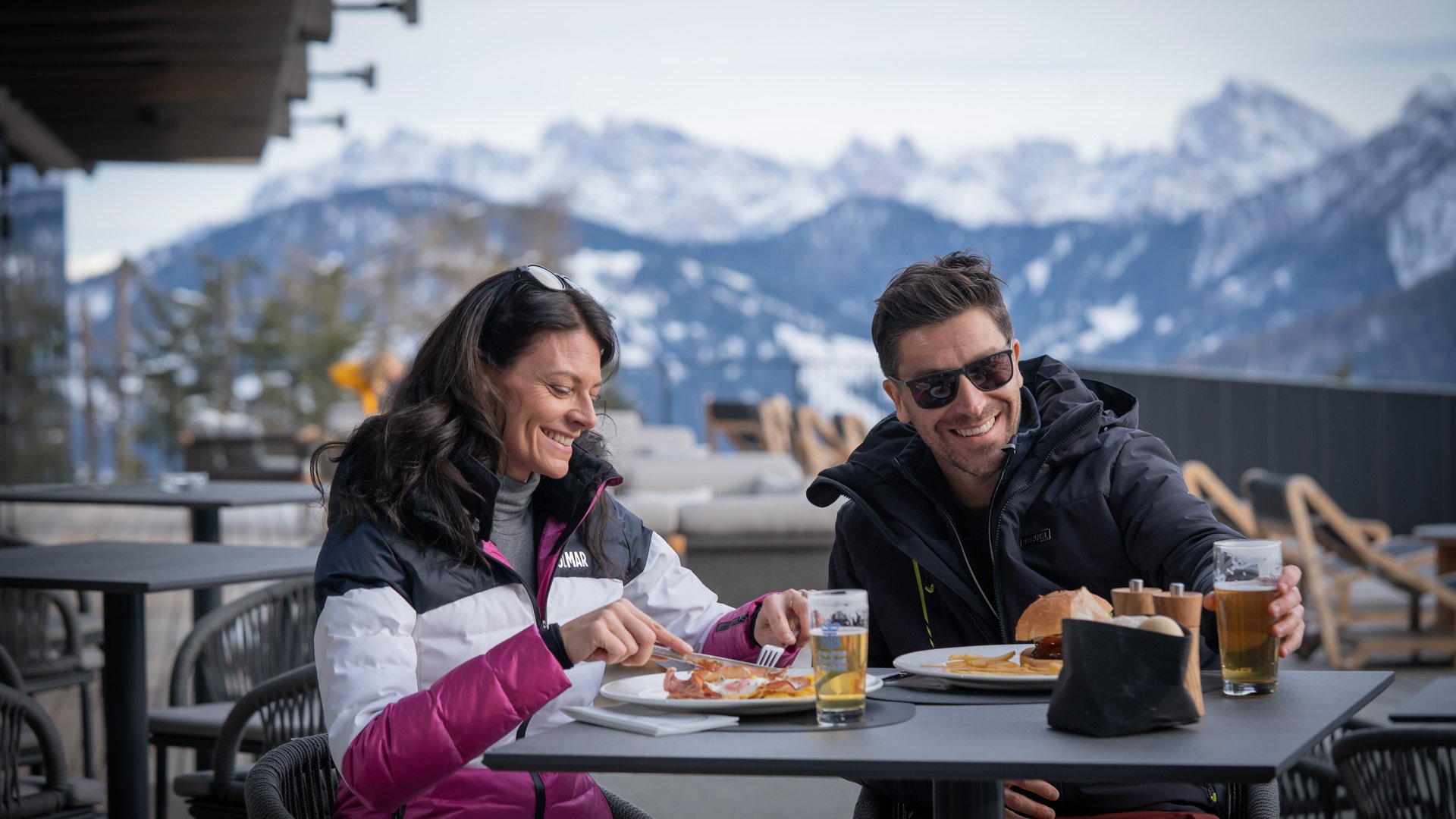 Hotel near Plan de Corones/Kronplatz: more flavour! Couple dining outdoors with snowy mountains in the background.