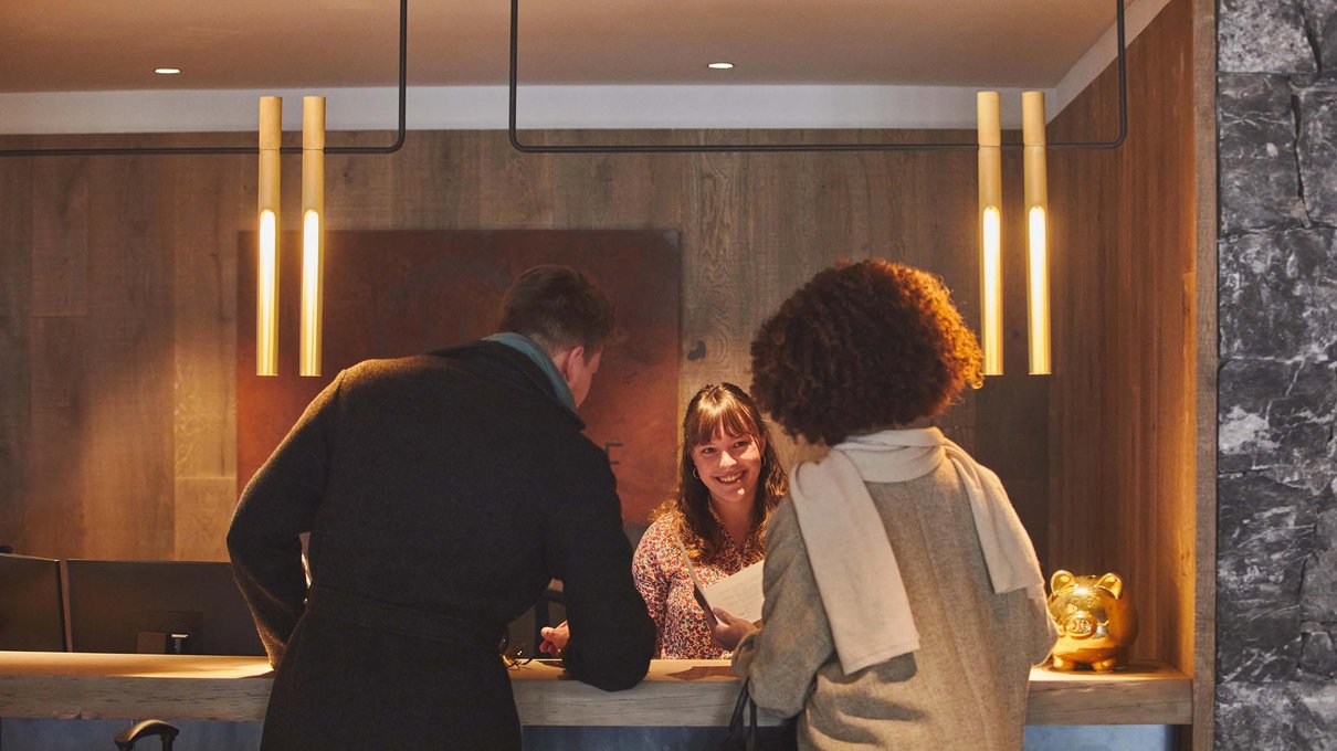 Deine Unterkunft im Pustertal: oh, wow! Personen sprechen mit der Rezeptionistin in einem modernen Hotel