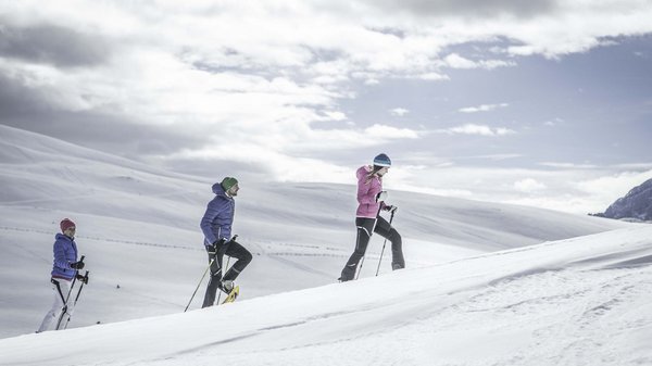 Kronplatz + Hotel an der Piste = Olangerhof Drei Personen machen Schneeschuhwandern in verschneiter Landschaft