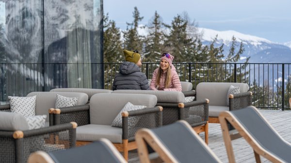 Kronplatz + Hotel an der Piste = Olangerhof Paar sitzt auf Sesseln auf verschneiter Bergterrasse