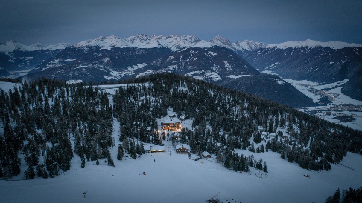 Deine Unterkunft im Pustertal: oh, wow! Beleuchtetes Hotel im Schnee mit verschneiten Bergen im Hintergrund bei Dämmerung
