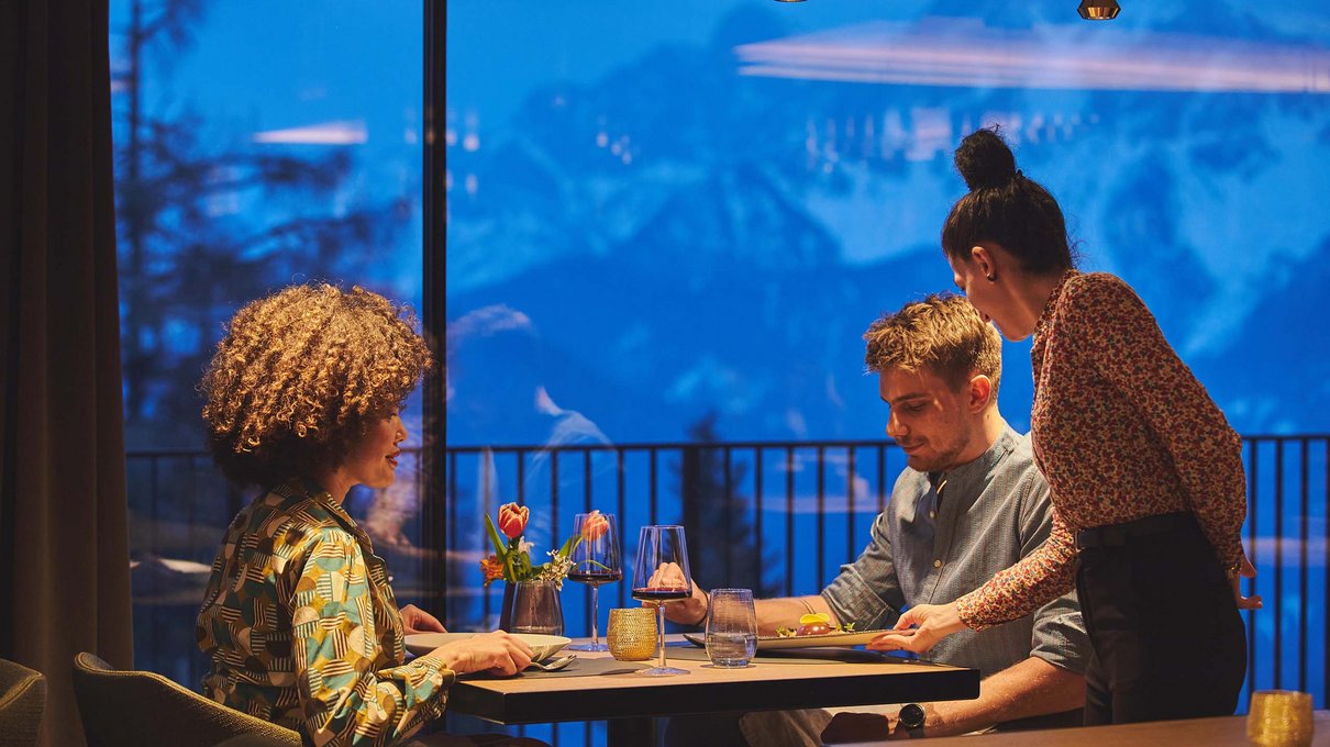 Deine Unterkunft im Pustertal: oh, wow! Paar wird im Restaurant mit Bergblick bei Sonnenuntergang bedient
