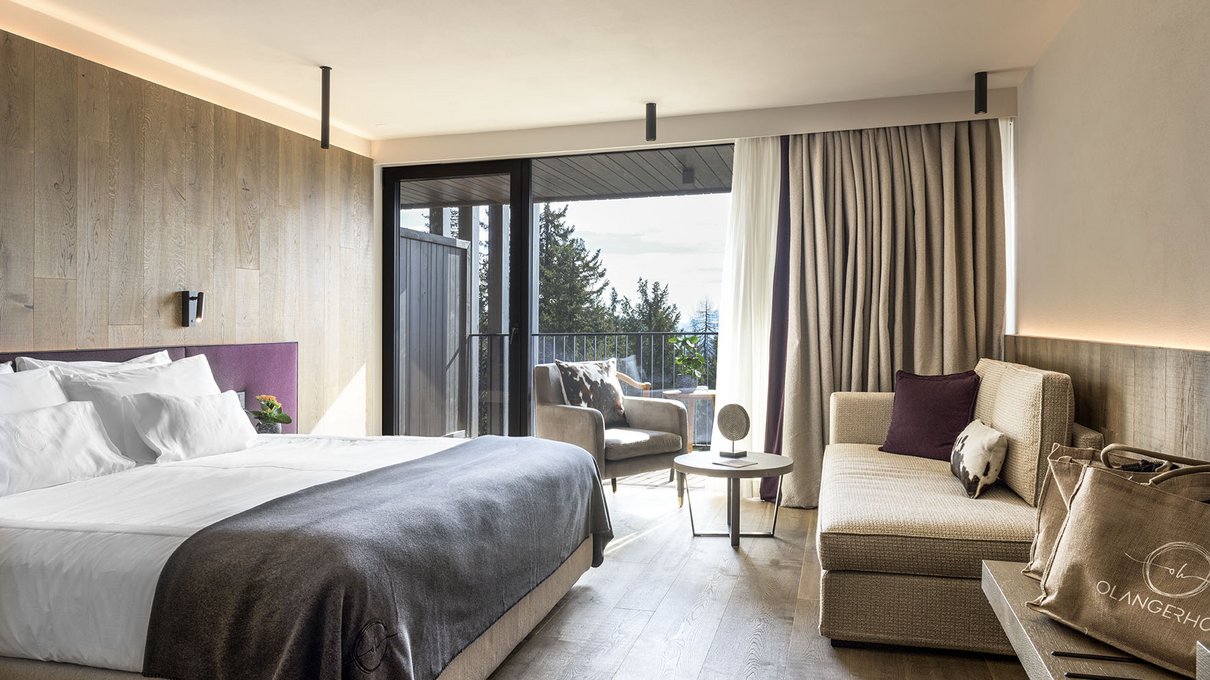 Deine Unterkunft im Pustertal: oh, wow! Modernes Hotelzimmer mit großem Bett, Sofa und Balkon mit Blick auf die Bäume