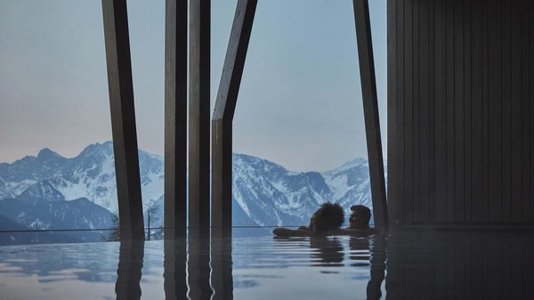 Hotel in Plan de Corones con piscina: il tuo Olangerhof Due persone rilassate in piscina con vista sulle montagne innevate