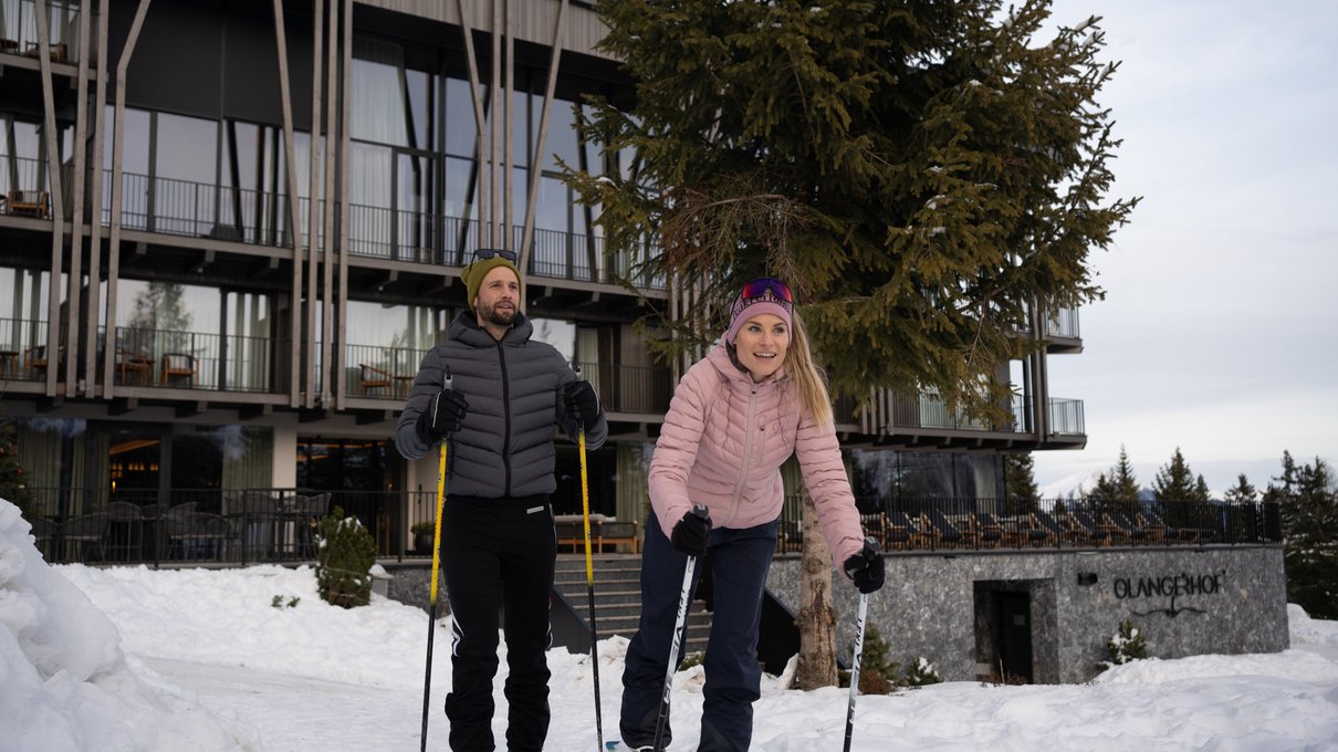 Deine Unterkunft im Pustertal: oh, wow! Zwei Personen beim Langlaufen vor einem modernen Gebäude im Schnee