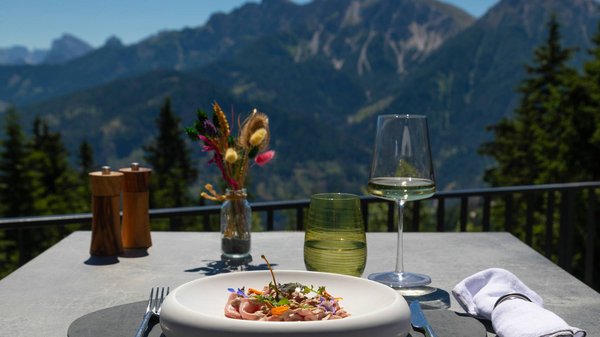 Hotels an der Piste in Südtirol mit Halbpension Gourmetgericht mit Weinglas auf Gartentisch mit Bergblick