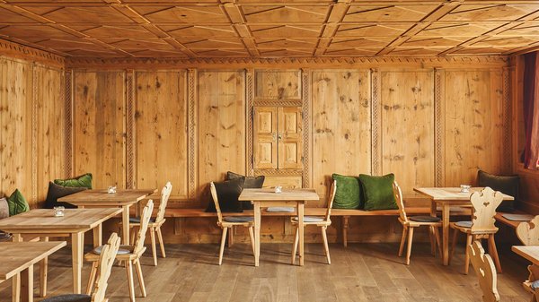 Hotels an der Piste in Südtirol mit Halbpension Innenraum mit Holzverkleidung, Holzstühlen und grünen Kissen