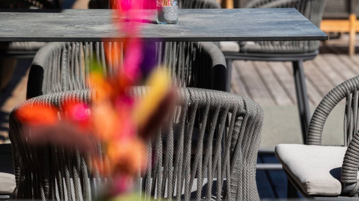 Deine Unterkunft im Pustertal: oh, wow! Tische mit bunten Blumen und grauen Stühlen in einem sonnigen Außenbereich