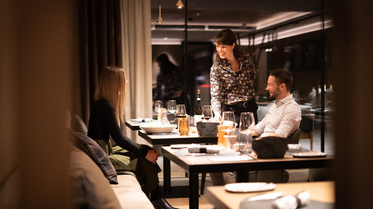 Deine Unterkunft im Pustertal: oh, wow! Kellnerin serviert zwei Gästen in einem eleganten Restaurant am Abend