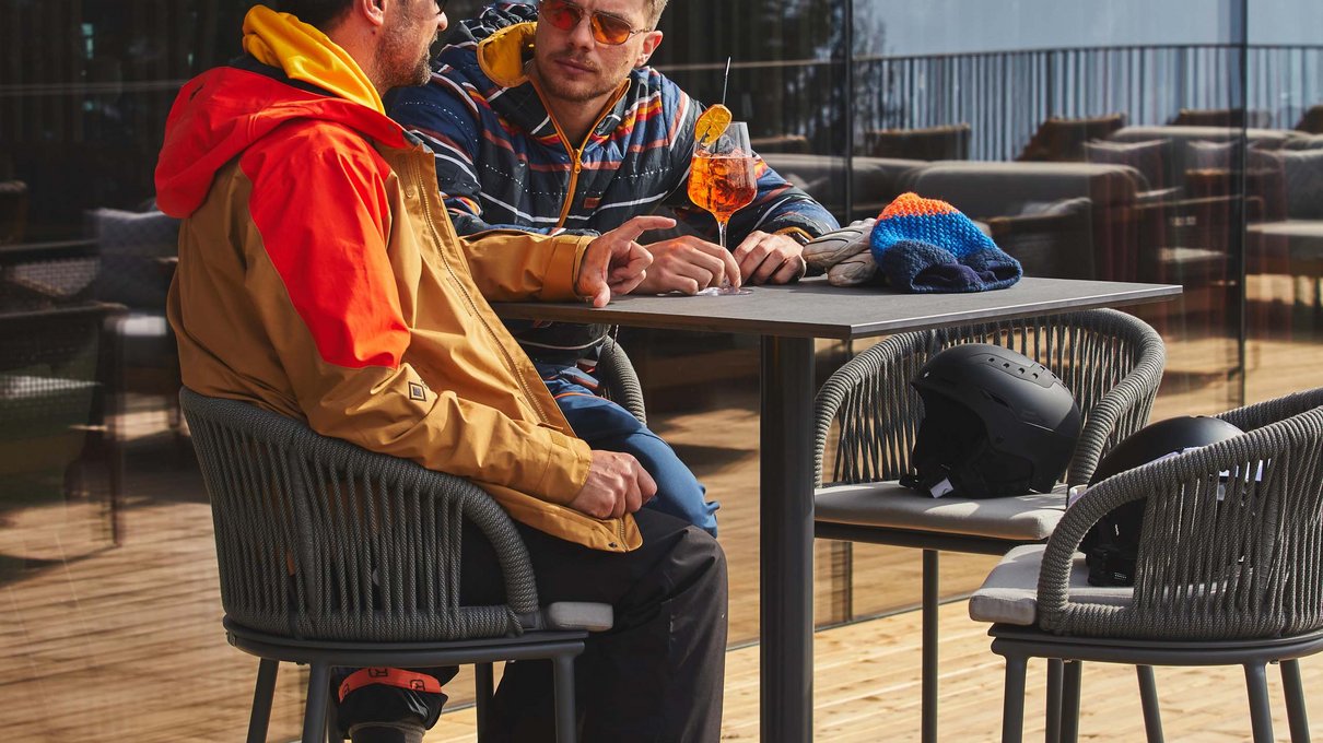 Deine Unterkunft im Pustertal: oh, wow! Zwei Männer in Skibekleidung sitzen draußen an einem Tisch mit Getränk und Skiausrüstung
