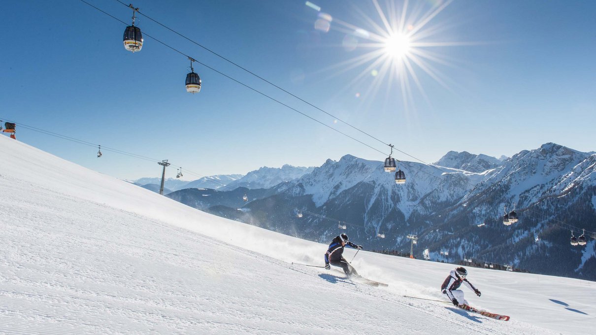 Deine Unterkunft im Pustertal: oh, wow! Skifahrer fahren eine verschneite Piste mit Bergen und Sessellift im Hintergrund hinunter