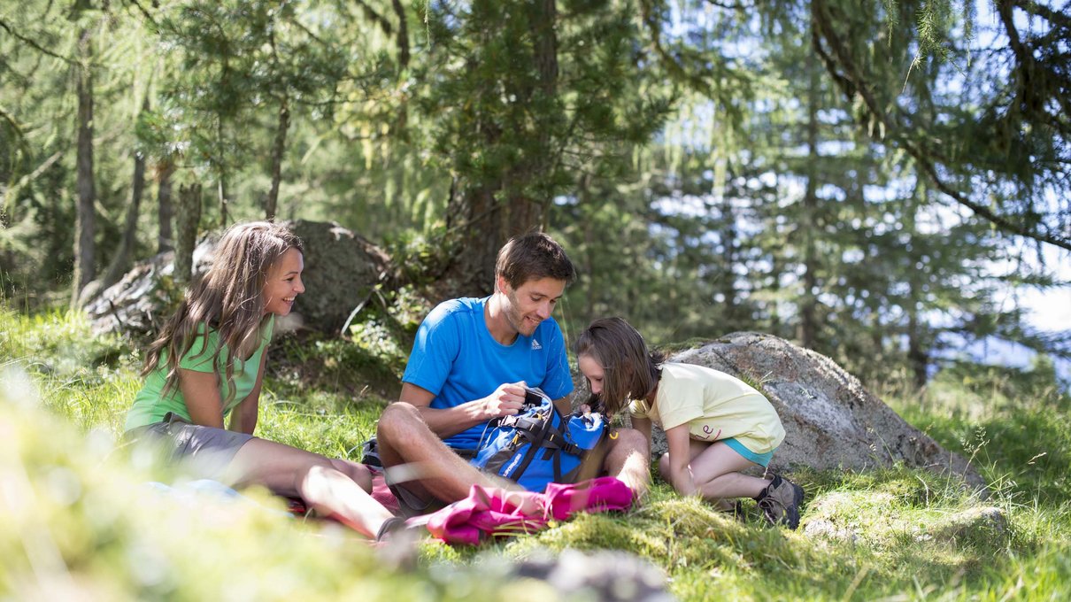 Deine Unterkunft im Pustertal: oh, wow! Familie entspannt sich und schaut in einen Rucksack beim Wandern im Wald