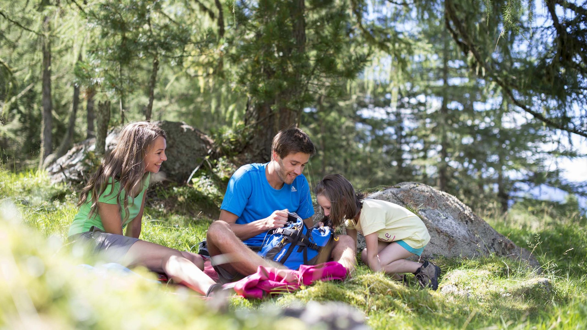 Olang in summer: sunny days at Olangerhof Family relaxing and looking into a backpack while hiking in the forest