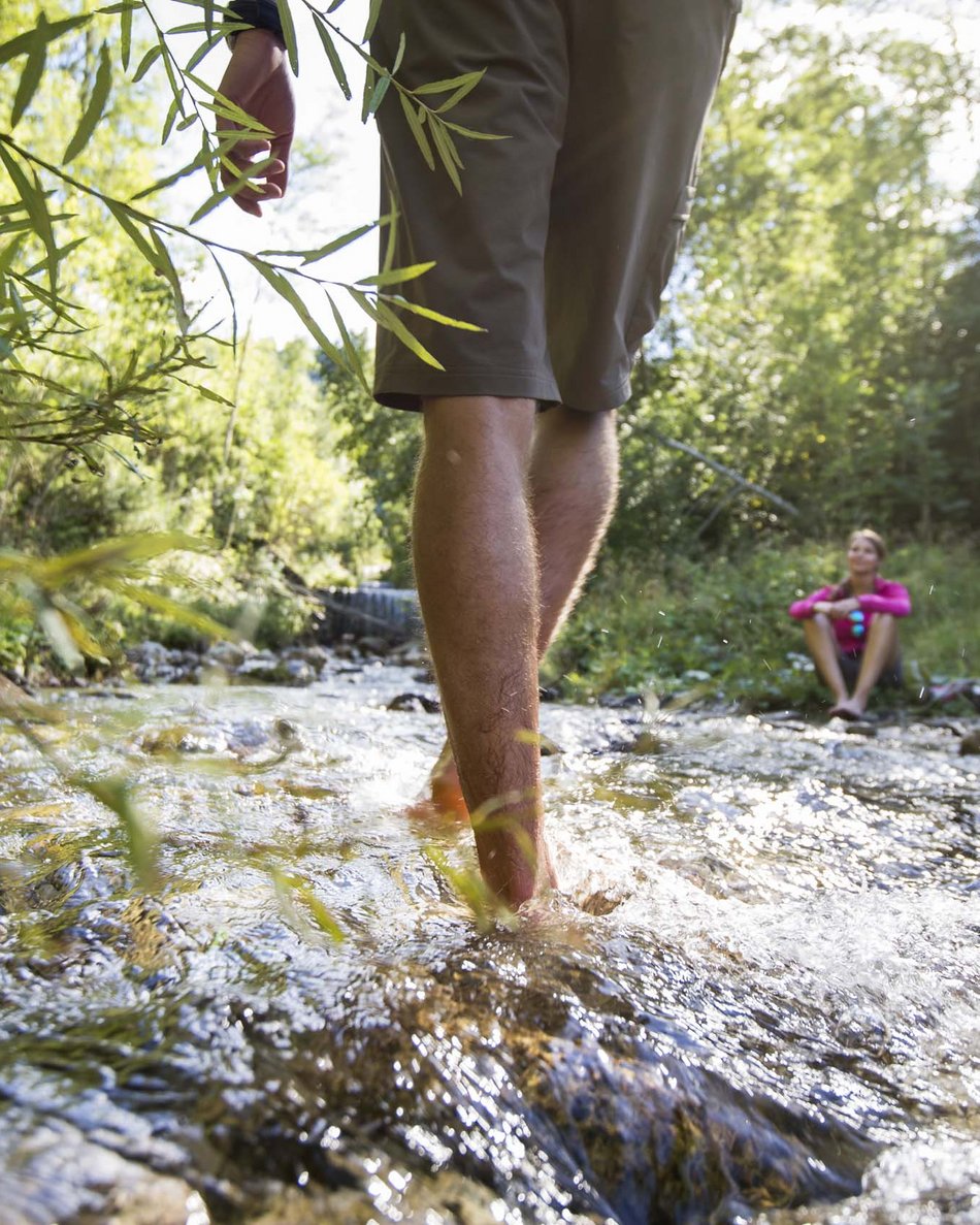 Al Plan de Corones: il tuo hotel ricco di attività Persona che attraversa un ruscello con acqua limpida in un bosco verde