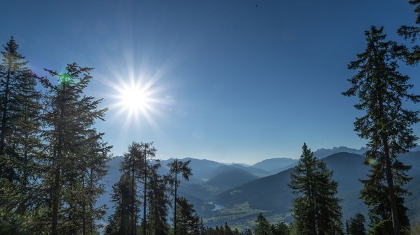 Dein Hotel in Olang: Willkommen im Olangerhof! Berglandschaft mit Bäumen und strahlender Sonne am blauen Himmel