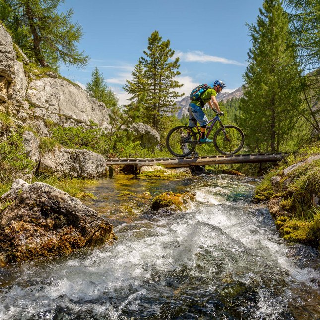 Il tuo hotel in Val Pusteria: Olangerhof Ciclista con casco attraversa ponte di legno su ruscello montano