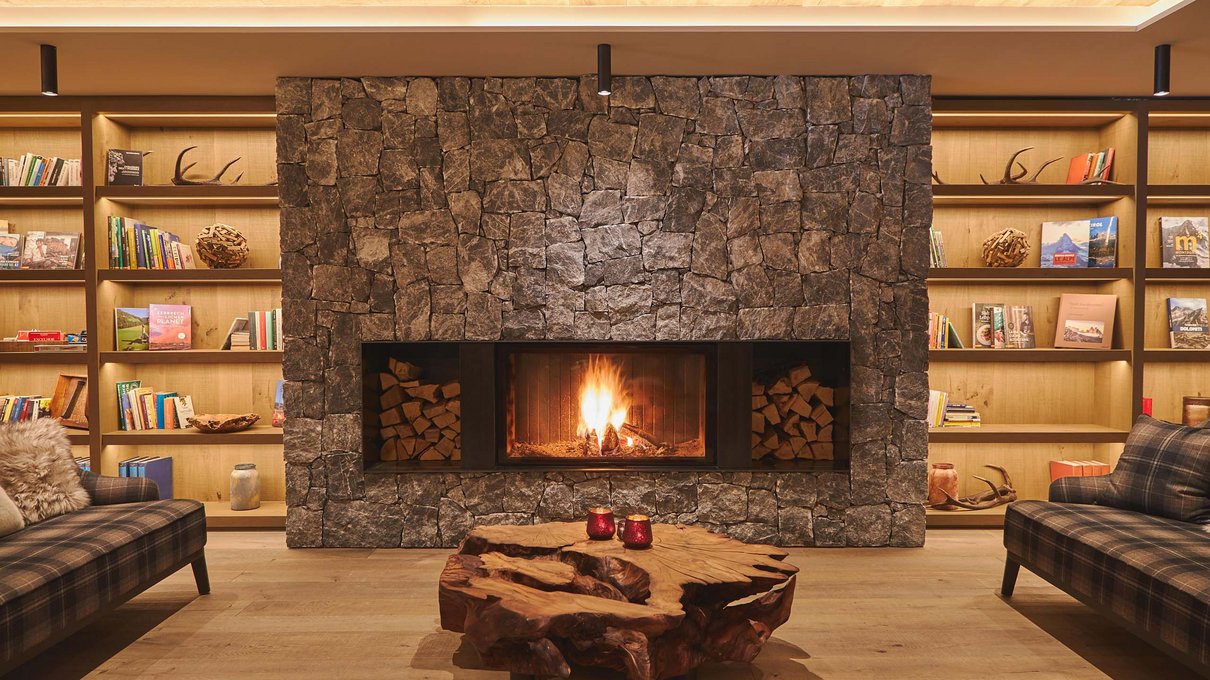 Deine Unterkunft im Pustertal: oh, wow! Wohnzimmer mit Kamin aus Stein, Bücherregalen und natürlichem Holztisch