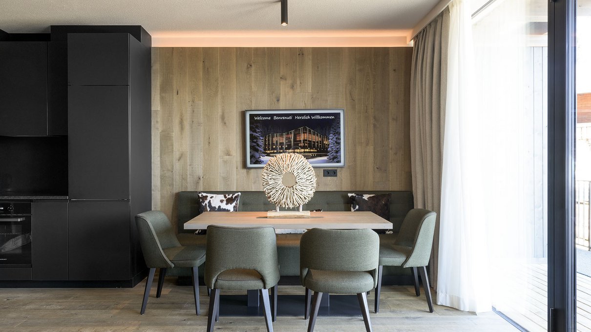 Deine Unterkunft im Pustertal: oh, wow! Moderner Wohnraum mit Tisch, grünen Stühlen und großem Fenster mit Vorhängen