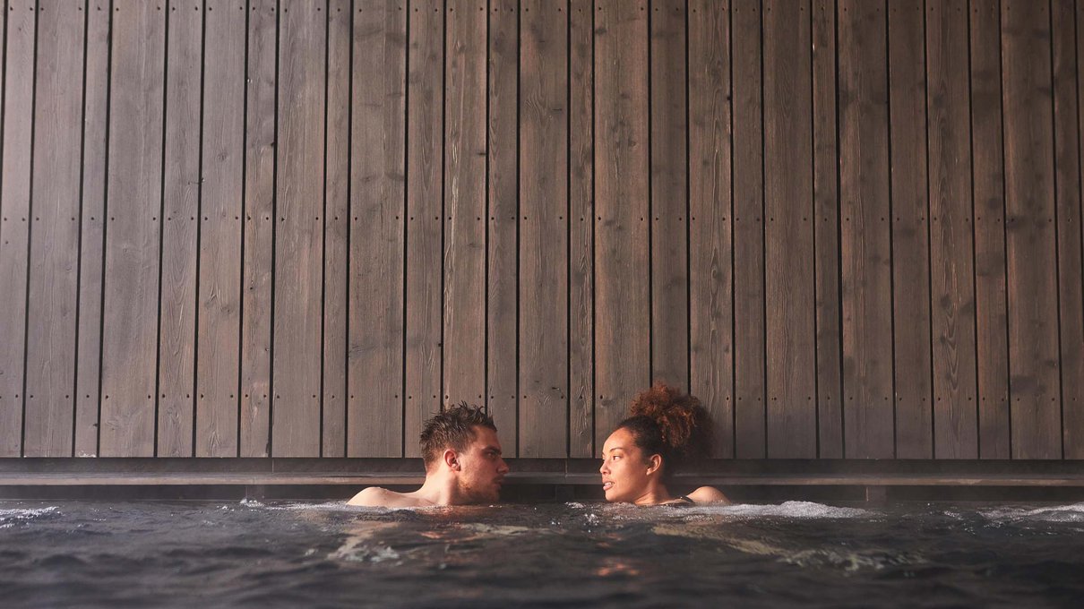 Deine Unterkunft im Pustertal: oh, wow! Zwei Personen entspannen in einem Whirlpool vor einer Holzwand