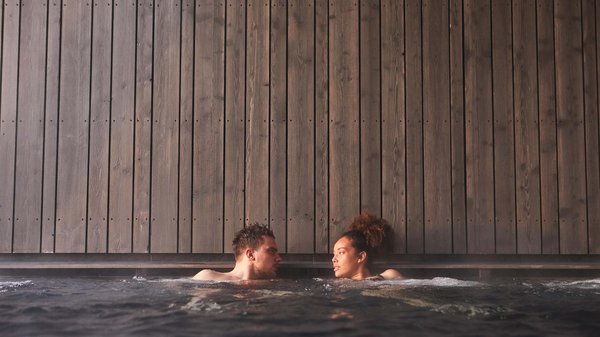 Dein Wellnesshotel am Kronplatz: Olangerhof Zwei Personen entspannen in einem Whirlpool vor einer Holzwand